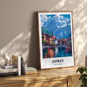 May include: A framed poster with a colorful illustration of a town in the Alps. The poster has the text "Annecy Les Alpes" at the bottom.