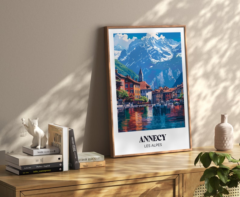 May include: A framed poster with a colorful illustration of a town in the Alps. The poster has the text "Annecy Les Alpes" at the bottom.