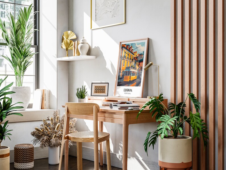 May include: A home office workspace with a wooden desk, chair, and a potted plant. The desk has a lamp, a framed print of a tram in Lisbon, Portugal, and a few books. There is a potted plant on the floor next to the desk.