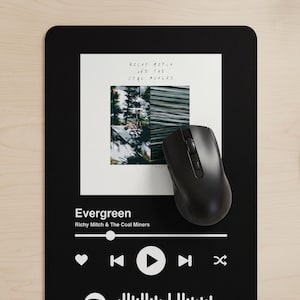Può includere: Un tappetino per mouse rettangolare nero con un design bianco da lettore musicale. Al centro è presente la copertina dell'album di Richy Mitch and the Coal Miners, con il titolo Evergreen e il nome dell'artista. Un mouse nero è appoggiato sopra.