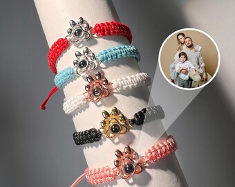 May include: Five colorful braided bracelets with a paw print charm. Each charm has a different colored eye. The bracelets are displayed on a white cylinder.