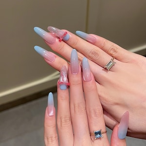 Könnte beinhalten: Lange, mandelförmige Nägel in Ombre-Optik in Hellblau und Rosa mit einem glitzernden Akzentnagel und einem rosa Schleifen-Akzentnagel.