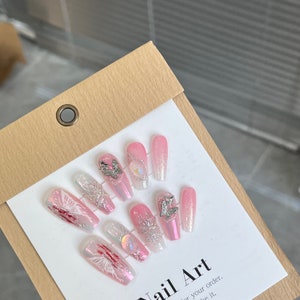 May include: Pink and white press-on nails with a butterfly design and glitter accents. The nails are displayed on a white card with the text "Nail Art" and "for your order."