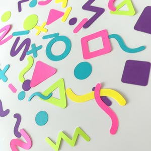 以下が含まれることがあります： ネオンピンク、ブライトイエロー、ライムグリーン、パープル、ティールカラーの紙製紙吹雪の詰め合わせ。円形、正方形、三角形、プラス記号、ジグザグ、波線などの形が、白い表面に散らばっています。
