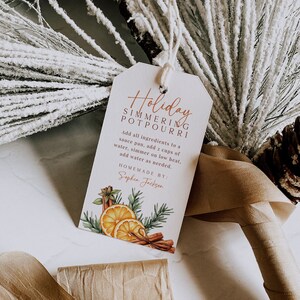 Könnte beinhalten: Ein weißes Etikett mit dem Text "Holiday Simmering Potpourri" in brauner Schrift. Das Etikett enthält Anweisungen zum Herstellen von Potpourri und lautet "Homemade by: Sophia Jackson". Das Etikett ist mit einer Aquarell-Illustration von Orangen, Zimtstangen und Kiefernzweigen verziert.