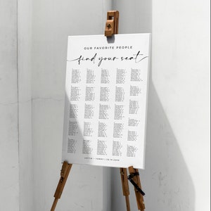 May include: A white wedding seating chart with black text. The chart is titled "Our Favorite People find your seat". The chart lists names and table numbers. The bottom of the chart reads "Lottie + Tommy | 28.10.20XX".