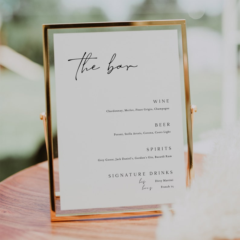 May include: A gold-framed sign with the text "The bar" at the top. The sign lists the drinks available, including wine, beer, spirits, and signature drinks. The signature drinks are "biz berg", "Dirty Martini", and "French 75".