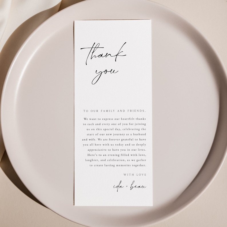 Op de afbeelding: Een eenvoudige witte bedankkaart met zwarte kalligrafie. De tekst luidt "Dank je wel" in een groot handschrift en "Aan onze familie en vrienden." in een kleiner lettertype. De tekst gaat verder met een boodschap van dankbaarheid voor het bijwonen van de bruiloft en het vieren van de nieuwe reis van het paar als man en vrouw. De kaart is ondertekend met "Met liefde, ida-beau".