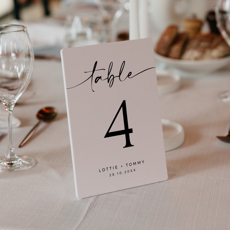 May include: White table number card with black calligraphy that says "table 4" and the text "Lottie + Tommy 28.10.20XX"