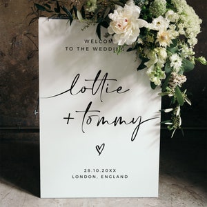 May include: White wedding welcome sign with black calligraphy text that reads "Welcome to the Wedding Lottie + Tommy" with a small heart symbol and the date "28.10.20XX" and the location "London, England".