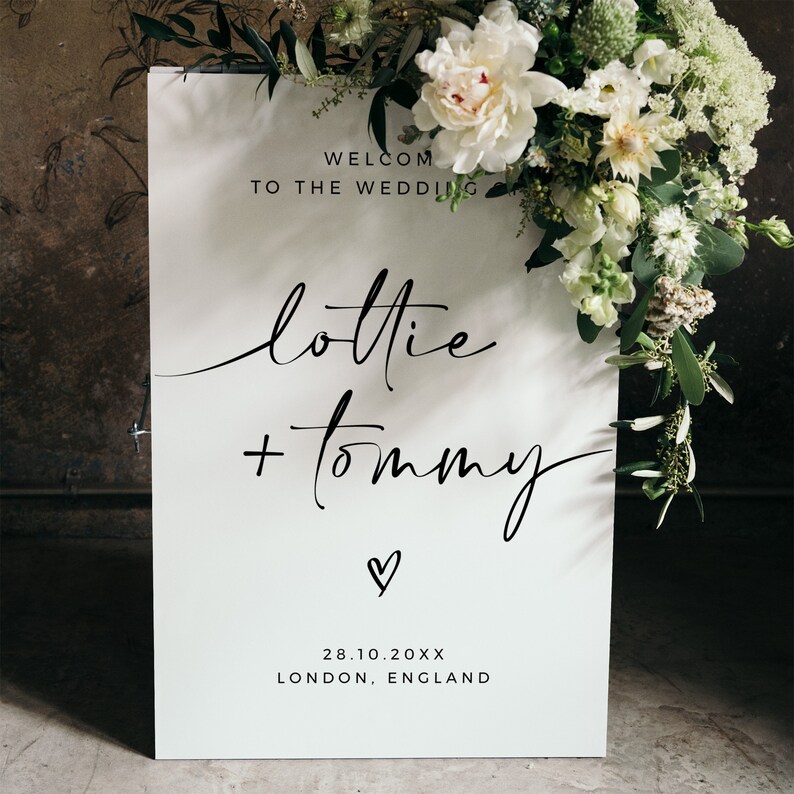 May include: White wedding welcome sign with black calligraphy text that reads "Welcome to the Wedding Lottie + Tommy" with a small heart symbol and the date "28.10.20XX" and the location "London, England".