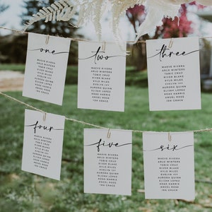 May include: Six white cards with black calligraphy hanging from a string. Each card has a number from one to six and a list of names. The names include Maeve Rivera, Arlo Winters, Tobie Cruz, River Blake, Kylo Miles, Evelyn Ivy, Aurora Quinn, Elijah Lopez, Koas Harris, Angel Rose, and Ida Grace.