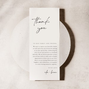 Op de afbeelding: Een eenvoudige bedankkaart met een handgeschreven boodschap die dankbaarheid uitdrukt aan familie en vrienden. De kaart bevat de tekst "Dank je" in een handschrift en de boodschap "Aan onze familie en vrienden. We willen onze oprechte dank uitspreken aan elk van jullie voor het bijwonen van deze speciale dag, ter ere van de start van onze nieuwe reis als man en vrouw. We zijn voor altijd dankbaar dat jullie allemaal vandaag hier bij ons zijn en we waarderen het enorm om jullie in ons leven te hebben. Op een avond vol liefde, lachen en vieringen, terwijl we samenkomen om blijvende herinneringen te cre&euml;ren. Met liefde, ida + beau."