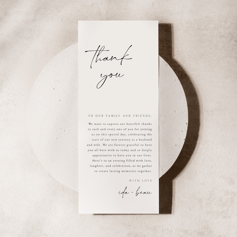 Op de afbeelding: Een eenvoudige bedankkaart met een handgeschreven boodschap die dankbaarheid uitdrukt aan familie en vrienden. De kaart bevat de tekst "Dank je" in een handschrift en de boodschap "Aan onze familie en vrienden. We willen onze oprechte dank uitspreken aan elk van jullie voor het bijwonen van deze speciale dag, ter ere van de start van onze nieuwe reis als man en vrouw. We zijn voor altijd dankbaar dat jullie allemaal vandaag hier bij ons zijn en we waarderen het enorm om jullie in ons leven te hebben. Op een avond vol liefde, lachen en vieringen, terwijl we samenkomen om blijvende herinneringen te cre&euml;ren. Met liefde, ida + beau."