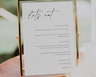 Op de afbeelding: Een gouden menukaart met de tekst "let's eat" bovenaan. Het menu bevat voorgerechten, hoofdgerechten en desserts. De voorgerechten omvatten mozzarella, cherrytomaatjes, basilicum en balsamico-glazuur, evenals baguette-plakjes met tomaat, basilicum, olijventapenade en geroosterde rode peper. De hoofdgerechten omvatten geroosterde kip gemarineerd in een pittige citroen- en kruidensaus, geserveerd met wilde rijstpilaf en groenten, en zalmfilets gecoat met verse kruiden en geserveerd met citroensaus. De desserts omvatten de bruidstaart en koffie en thee.