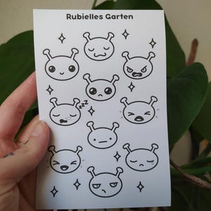 Könnte beinhalten: Ein weißes Stickerbogen mit schwarz-weißen Alien-ähnlichen Charakteren mit verschiedenen Gesichtsausdrücken und Diamantakzenten. Der Text "Rubielles Garten" ist oben aufgedruckt.