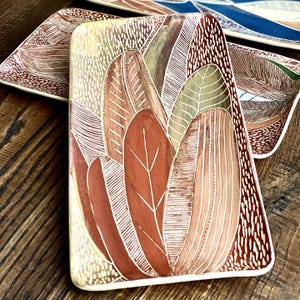 May include: A rectangular ceramic serving dish with a white rim and a design of stylised leaves in shades of red, brown, and green.