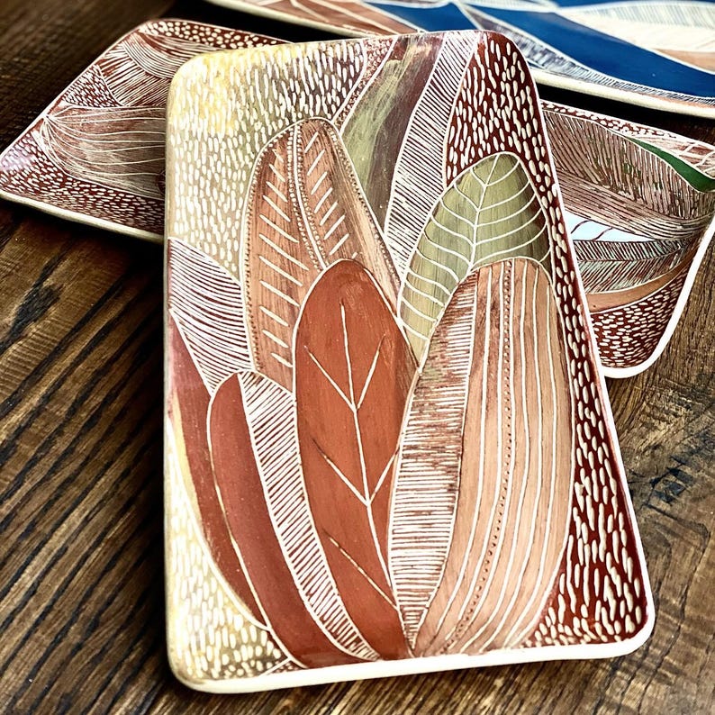 May include: A rectangular ceramic serving dish with a white rim and a design of stylised leaves in shades of red, brown, and green.