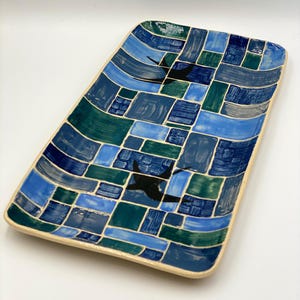 May include: A rectangular ceramic serving tray with a blue, green and white mosaic pattern. The tray features two black silhouettes of birds in flight.