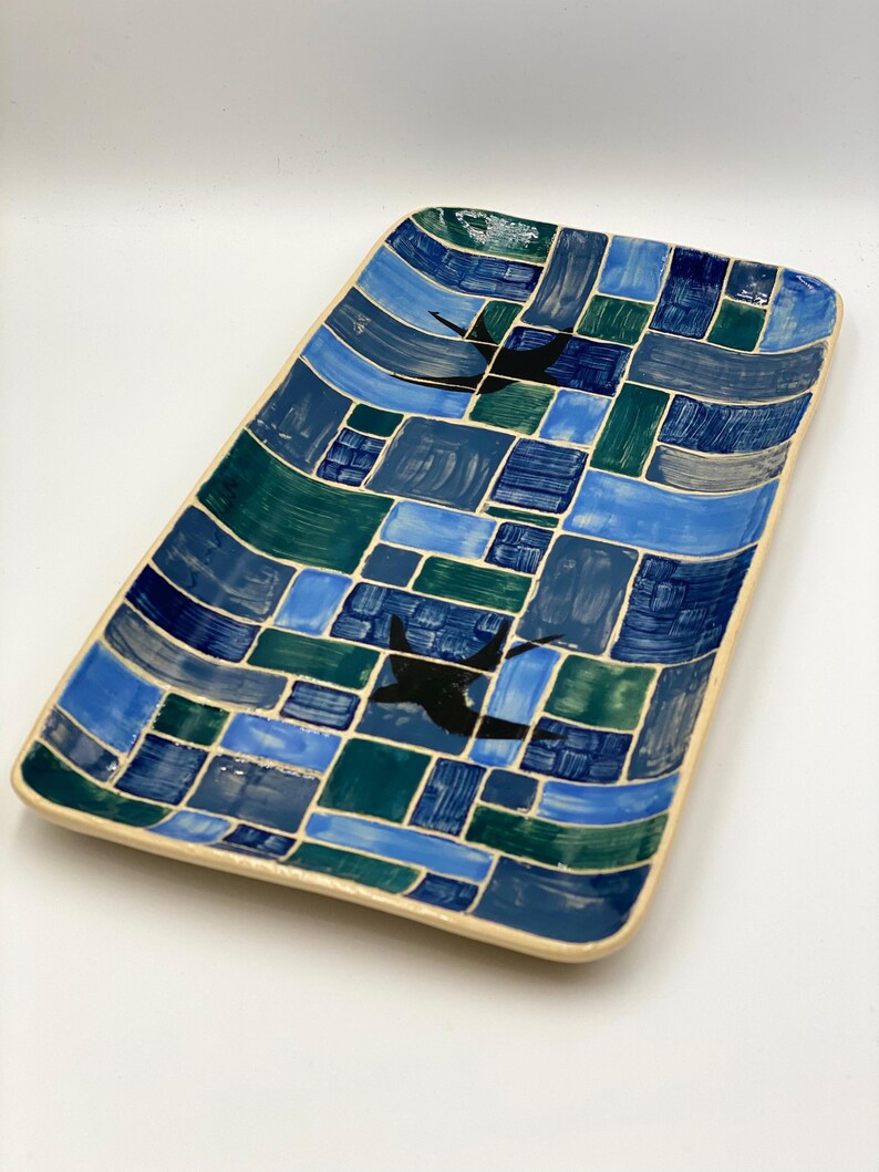 May include: A rectangular ceramic serving tray with a blue, green and white mosaic pattern. The tray features two black silhouettes of birds in flight.