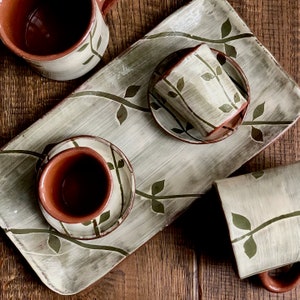 May include: A set of three ceramic mugs with a leafy design on a white background. The mugs are brown on the inside and have a brown rim. The mugs are on a white tray with a leafy design.