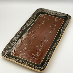May include: A rectangular ceramic serving tray with a brown base and black and white border. The tray features a design of stylised leaves in a dark brown colour.