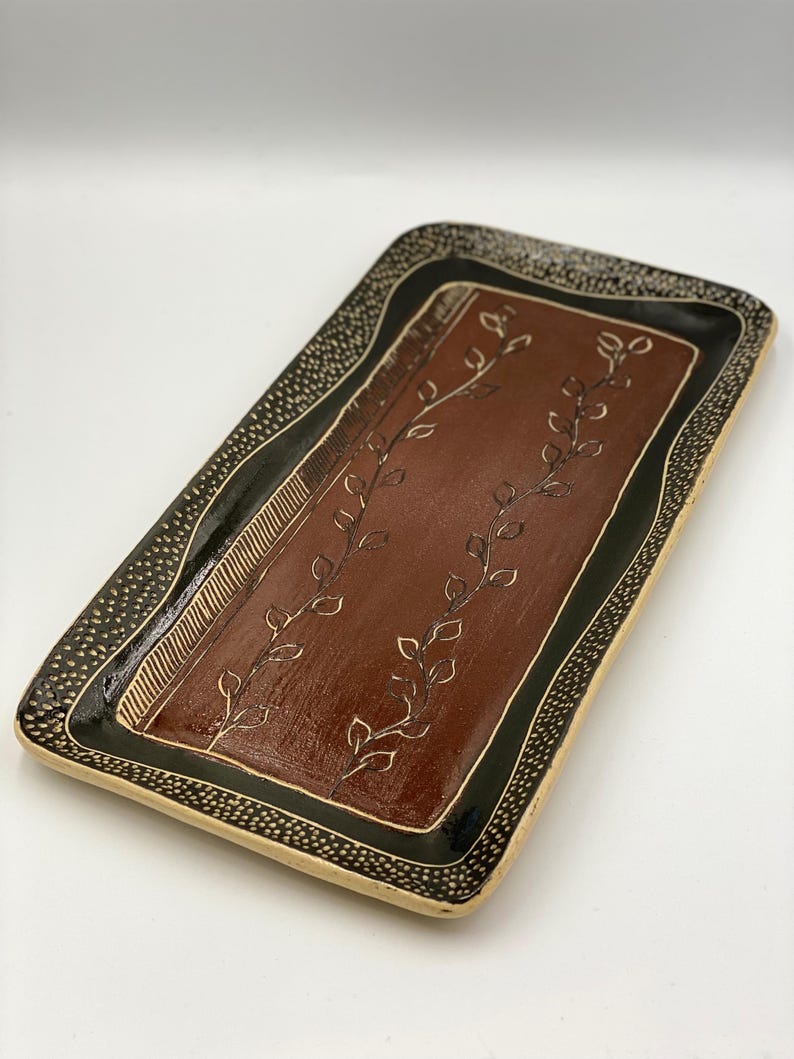 May include: A rectangular ceramic serving tray with a brown base and black and white border. The tray features a design of stylised leaves in a dark brown colour.