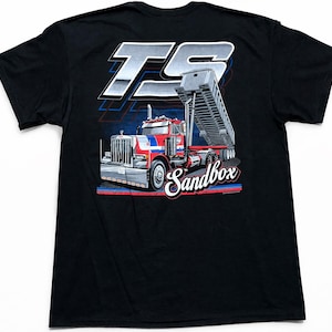 May include: Black t-shirt featuring a graphic of a red, white, and blue dump truck with the word "Sandbox" in a stylized font. The shirt also has the letters "TS" in a silver and white design above the truck.