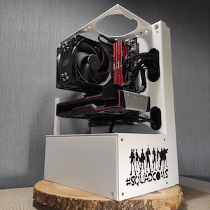 Könnte beinhalten: Ein weißes Computergehäuse mit einer schwarzen und roten Grafikkarte und einem schwarzen Lüfter. Das Gehäuse hat einen Aufkleber auf der Vorderseite, auf dem "#SquadGoals" mit einer Silhouette einer Gruppe von Personen steht.