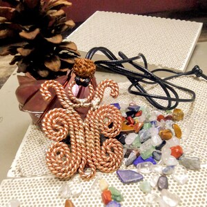 Peut inclure: Un pendentif en fil de cuivre en forme de papillon avec un cordon noir. Le pendentif est entouré de petites pierres colorées.
