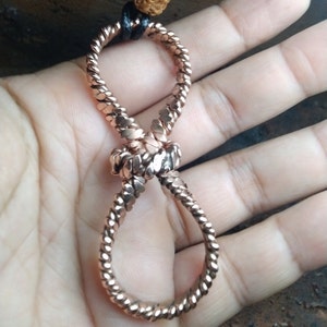 Puede incluir: Un collar con un símbolo de infinito de oro rosa hecho de alambre trenzado. El collar está atado en un nudo en el centro.
