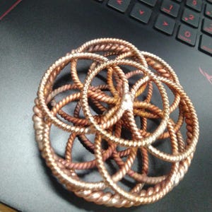 Könnte beinhalten: Ein kupferfarbenes Metall-Lebensblume-Mandala mit runder Form und kompliziertem Design.