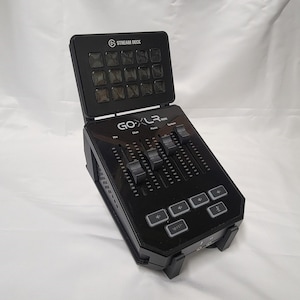 May include: Black Stream Deck Mini audio mixer with multiple faders, buttons, and a top panel with 15 illuminated buttons. The mixer has the text "GO XLR Mini" and "Stream Deck" printed on it. The device is designed for audio control.