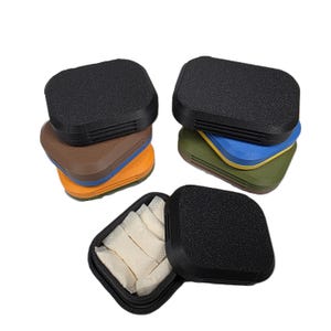 May include: Several small, rectangular, textured black cases with colorful bases are stacked and displayed. One case is open, revealing several white pouches. The cases have a simple, modern design and appear to be made of a durable material.