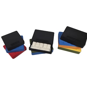 May include: A collection of black, rectangular boxes with a hinged lid, stacked on top of colorful, rectangular bases. One box is open, revealing white rectangular objects inside. The bases are red, blue, green, orange, and yellow.