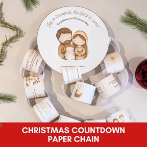 May include: A Christmas countdown paper chain with a circular centerpiece featuring a family illustration. The chain includes daily prompts. A red ornament and star-shaped decoration are also visible.