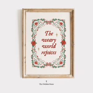 May include: A framed print featuring the words "The weary world rejoices" in red script. The text is encircled by a decorative border of green leaves, red poinsettias, and red ribbons. The frame is light brown.