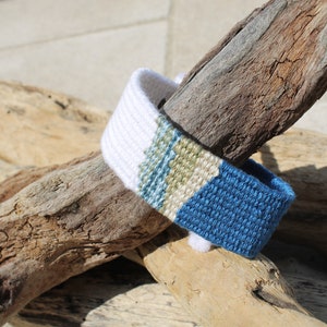Handwoven bracelet-half white and half ocean blue base with blue, green, beize elements in center image 1