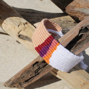 Handwoven bracelet-half white and half beize base with maroon, purple, pink and orange elements in center image 1