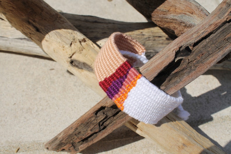 Handwoven bracelet-half white and half beize base with maroon, purple, pink and orange elements in center image 1