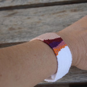 Handwoven bracelet-half white and half beize base with maroon, purple, pink and orange elements in center image 4