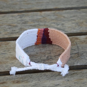 Handwoven bracelet-half white and half beize base with maroon, purple, pink and orange elements in center image 3