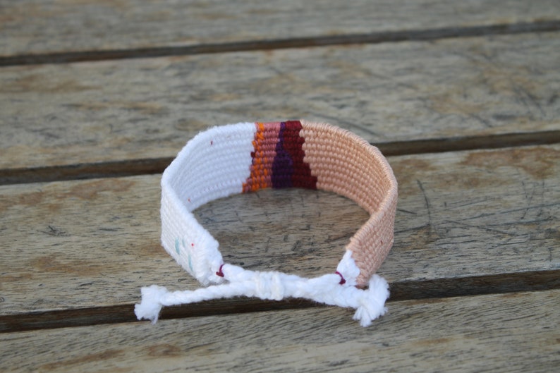 Handwoven bracelet-half white and half beize base with maroon, purple, pink and orange elements in center image 3