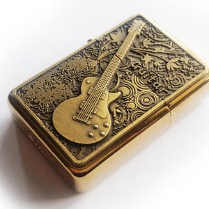 May include: A gold-tone lighter with an embossed design of a guitar and the word "Guitar" on the front.