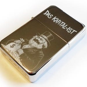 May include: A silver lighter with an engraved image of Karl Marx holding a bag of money. The text "Das Kapital-Ist" is engraved on the top of the lighter.
