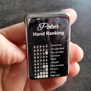 Può includere: Un accendino nero e argento con la scritta bianca "Poker Hand Ranking". L'accendino mostra una tabella di classificazione delle mani di poker con simboli di carte e nomi di mani.