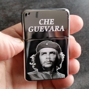 May include: Black lighter with the white text "CHE GUEVARA". The lighter has a black and white image of Che Guevara wearing a beret. The lighter is held in a hand.
