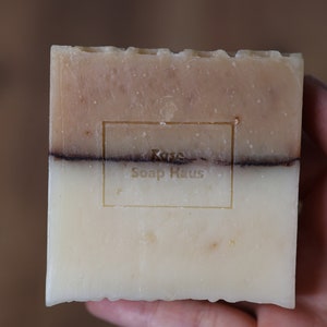 May include: A bar of soap with a brown and white swirl design. The soap has a label that reads "Rose Soap Haus".