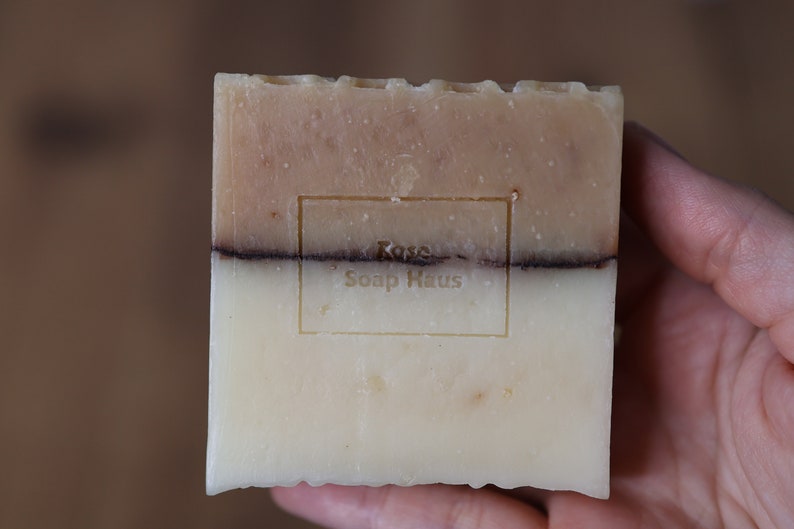 May include: A bar of soap with a brown and white swirl design. The soap has a label that reads "Rose Soap Haus".