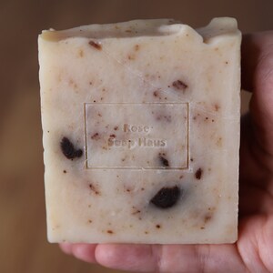 May include: A white bar of soap with brown flecks and the text "Rose Soap Haus" stamped on the front.